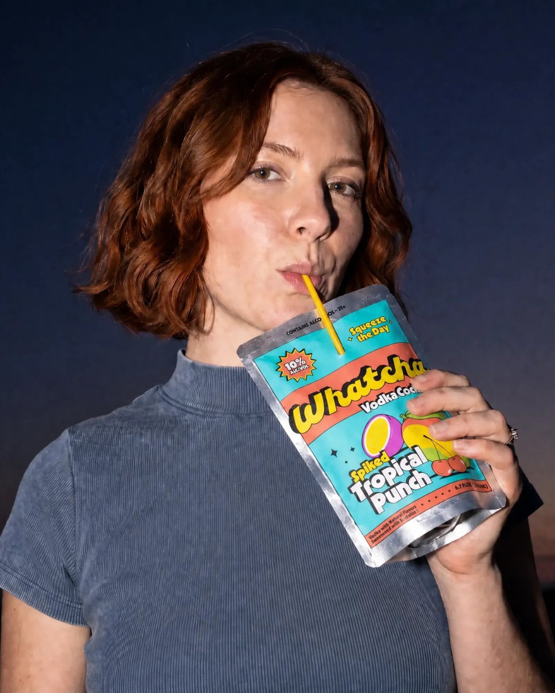Woman sipping a Whatcha Spiked Tropical Punch pouch at dusk